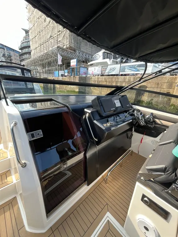 Interior view of a modern boat showing the helm area, control panel, and cockpit floor with wood-like decking.